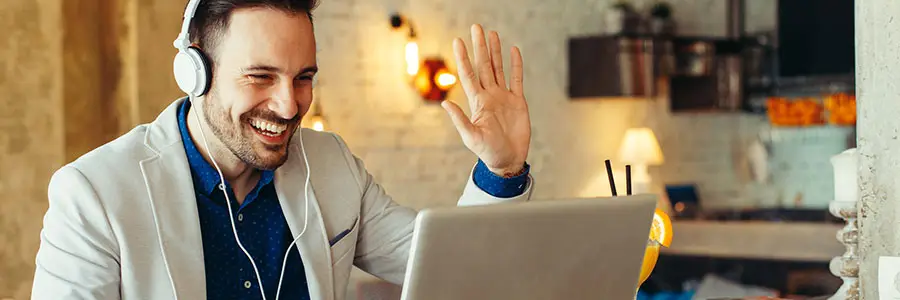 How to get the most out of Microsoft Teams – Managed IT Services, Consulting, and Support for Businesses and Non Profits Person wearing headphones and a blazer, waving while using a laptop in a modern workspace, illustrating remote communication and collaboration in Microsoft Teams.