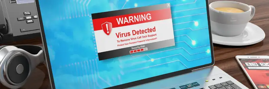2021August23Security_A_PH-LZl0TQ – Managed IT Services, Consulting, and Support for Businesses and Non Profits Laptop displaying a warning message about a virus detected, emphasizing cybersecurity risks, with a cup of coffee and a phone in the background.