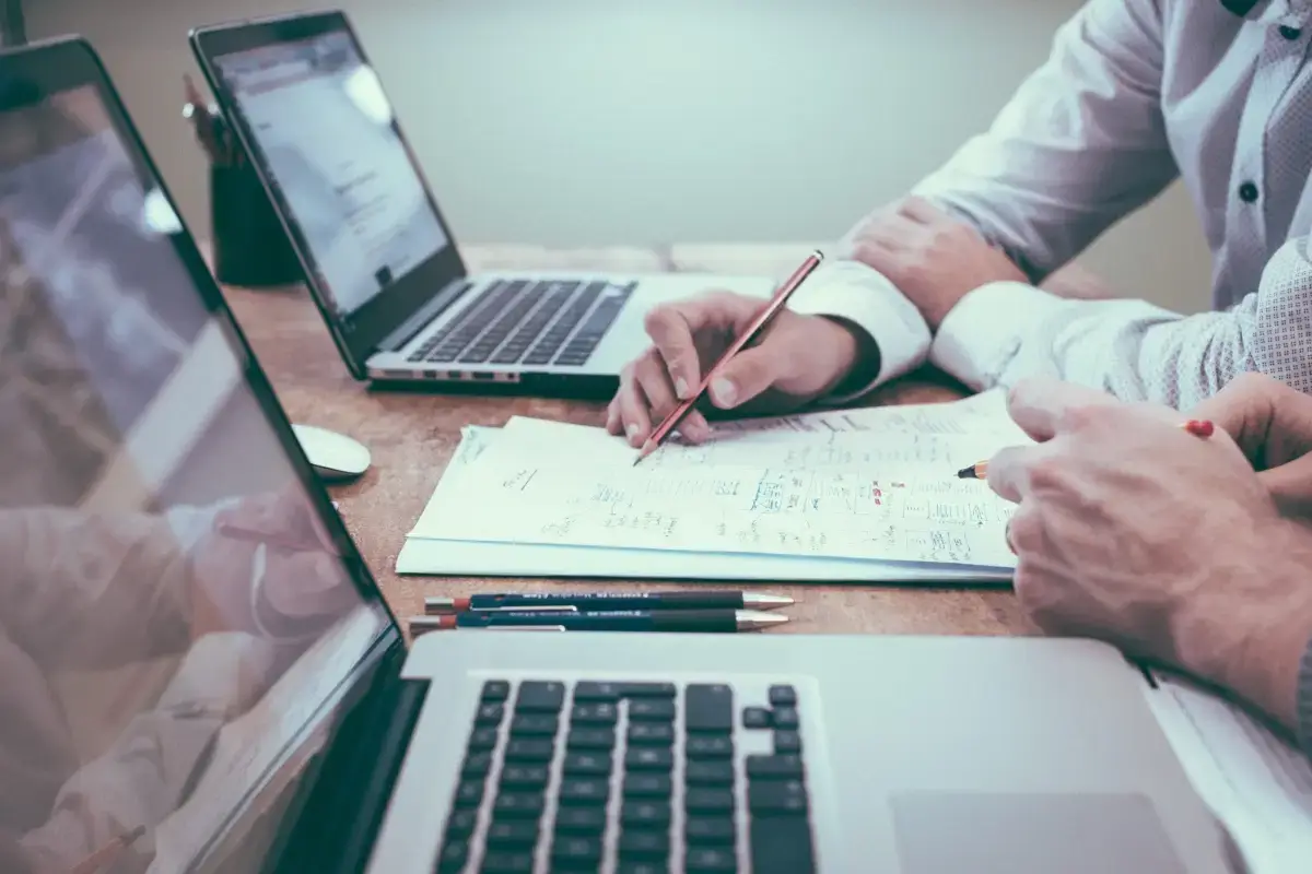 Solutions-by-need – Managed IT Services, Consulting, and Support for Businesses and Non Profits Two people collaborating at a desk with laptops, reviewing notes and sketches on paper, representing managed IT services for small businesses.